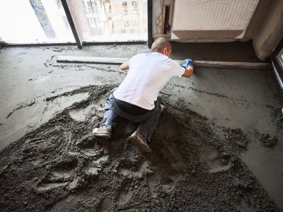Person glättet frischen Betonboden mit langer Latte, ebene Fläche entsteht durch präzises Ausrichten im Innenraum Person glättet frischen Betonboden mit langer Latte, ebene Fläche entsteht durch präzises Ausrichten im Innenraum