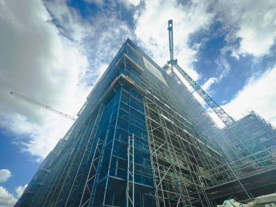 Hohes Gebäude eingerüstet, Kräne arbeiten daran, zeigt Fortschritt im Hochbau unter blauem Himmel mit Wolken Hohes Gebäude eingerüstet, Kräne arbeiten daran, zeigt Fortschritt im Hochbau unter blauem Himmel mit Wolken